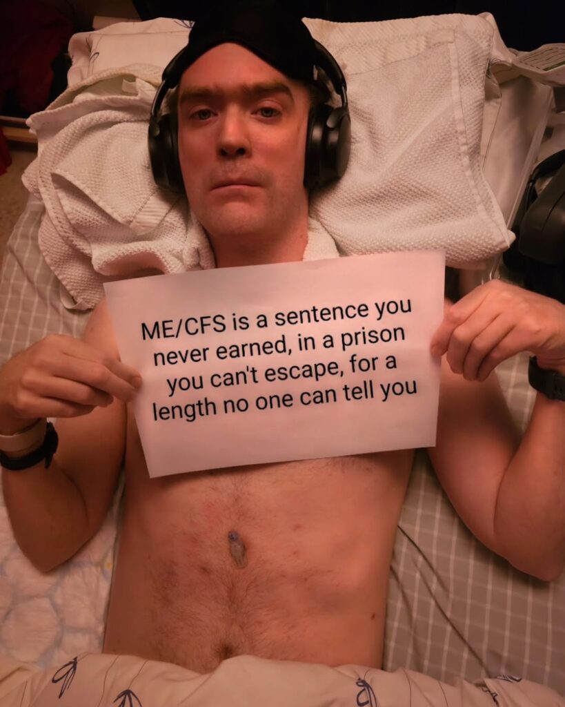 Eirik is holding a sign that reads: ME/CFS is a sentence you never earned, in a prison you can’t escape, for a length no one can tell you.