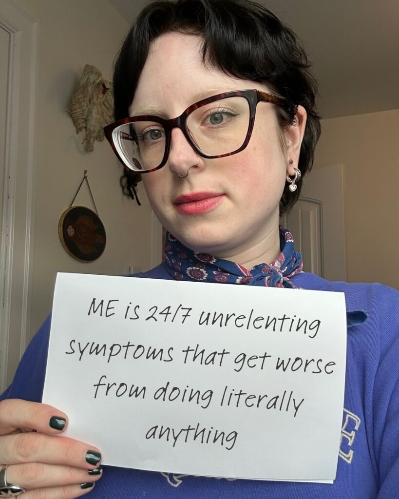 Katie is holding a sign that reads: “ME is 24/7 unrelenting symptoms that get worse from doing literally anything.”