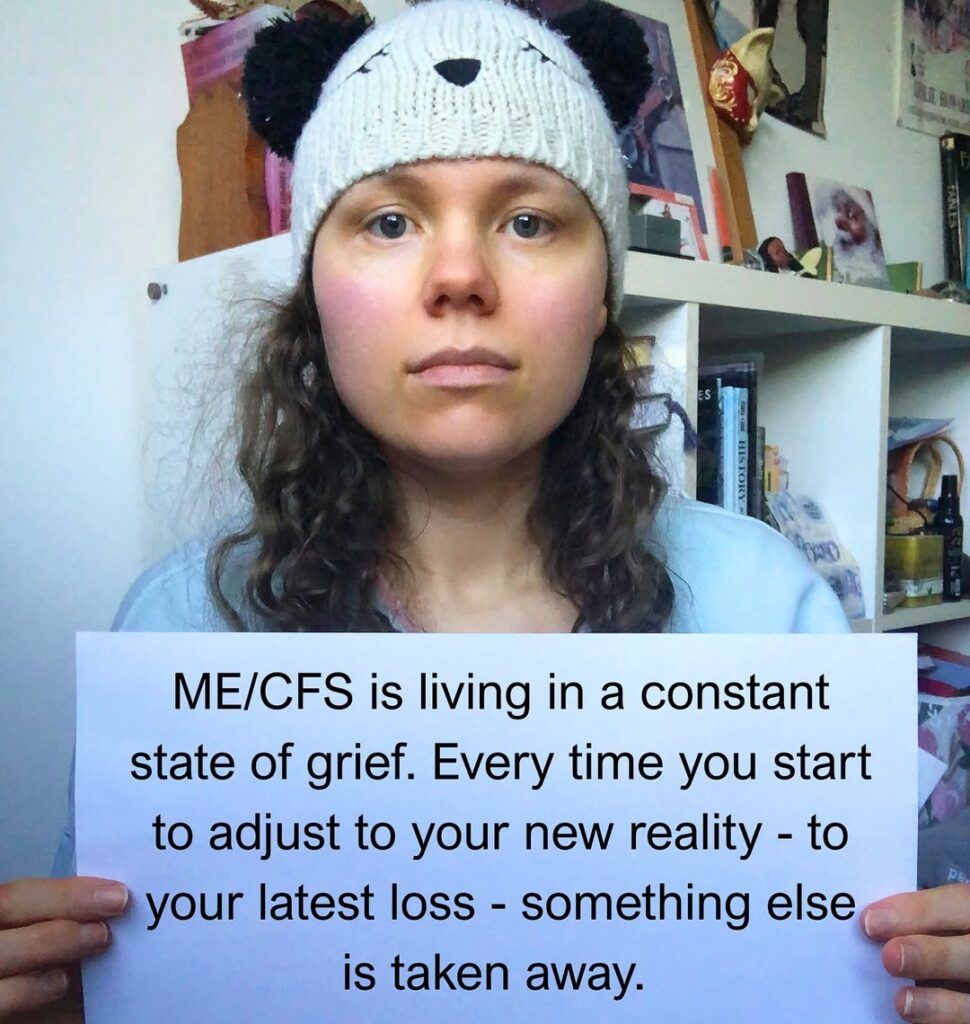 Liv is holding a sign that reads: ME/CFS is living in a constant state of grief. Every time you start to adjust to your new reality - to your latest loss - something else is taken away.