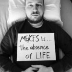 Niko is holding a sign that reads: ME/CFS is the absence of life.