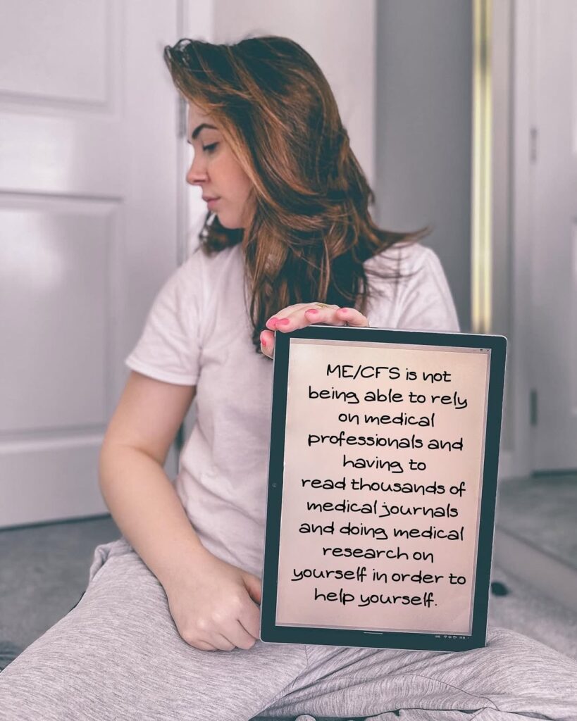 Laura is holding a sign that reads: ME/CFS is not being able to rely on medical professionals and having to read thousands of medical journals and doing medical research on yourself in order to help yourself.