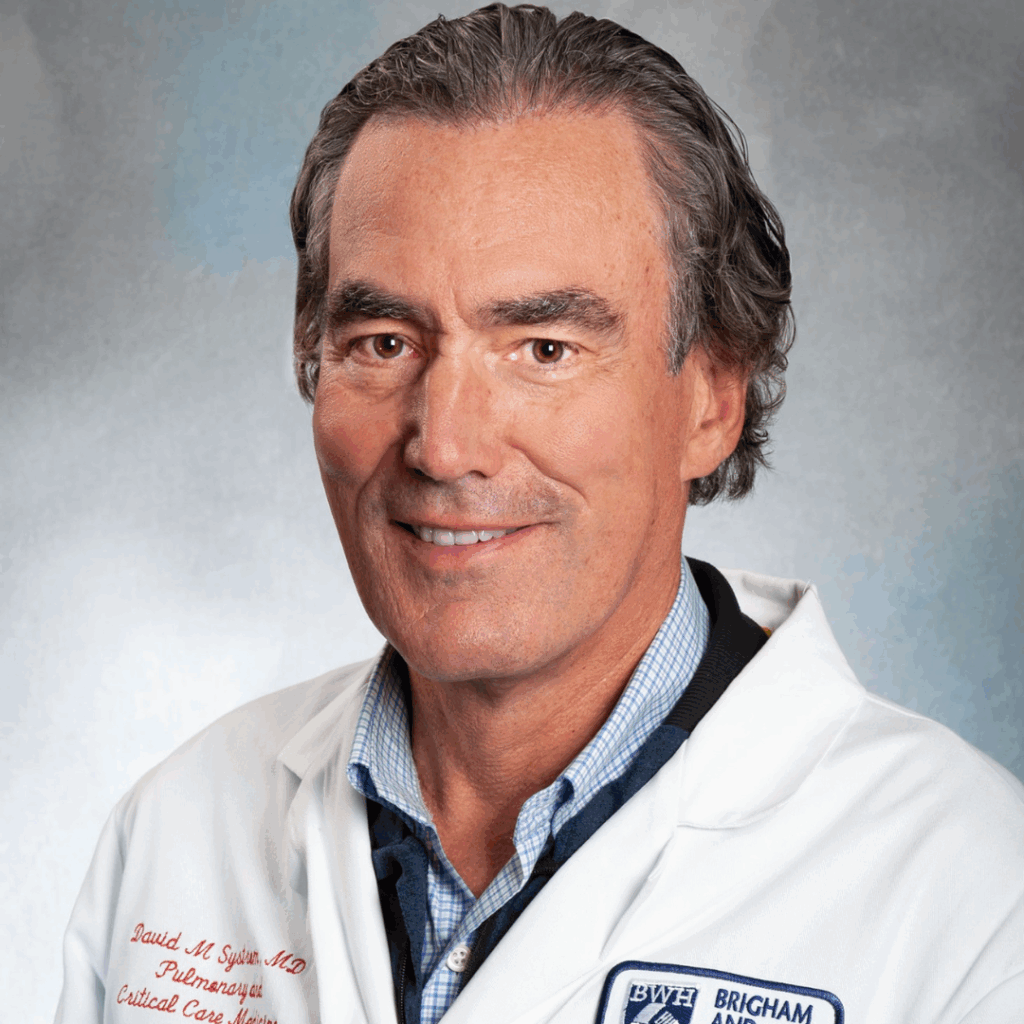 The image shows Dr. Systrom wearing a white medical coat. The coat has embroidery on the left chest area that reads: David M. Systrom, MD, Pulmonary and Critical Care Medicine.
